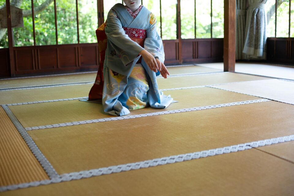 Maiko in a blue kimono performing a graceful gesture in a Kyoto tatami room