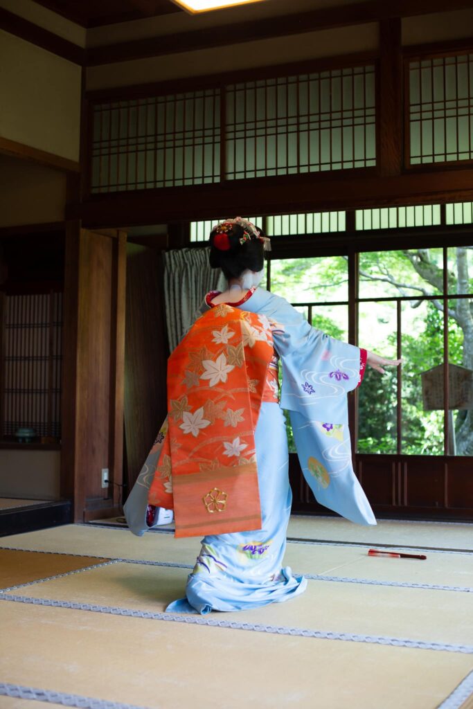 Maiko with a long orange darari obi dancing in a traditional Kyoto interior