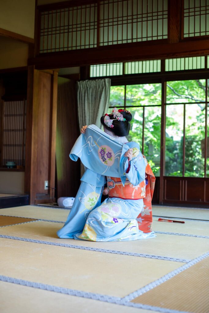 Kneeling maiko raising her kimono sleeve during a Kyoto dance performance