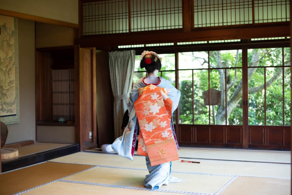 Maiko standing in a traditional Kyoto tatami room with hanging scroll and garden