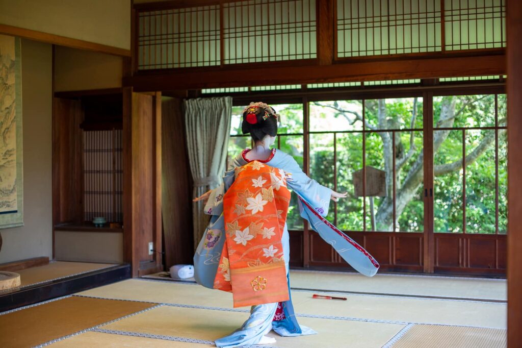 Maiko dancing with outstretched sleeves in a traditional Kyoto tatami room
