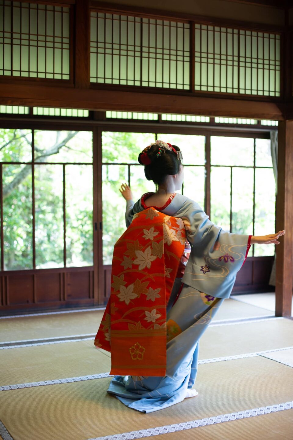 Maiko extending her arm in dance before garden windows in Kyoto